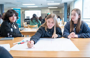 A group of three students at a table collaborating on a poster paper