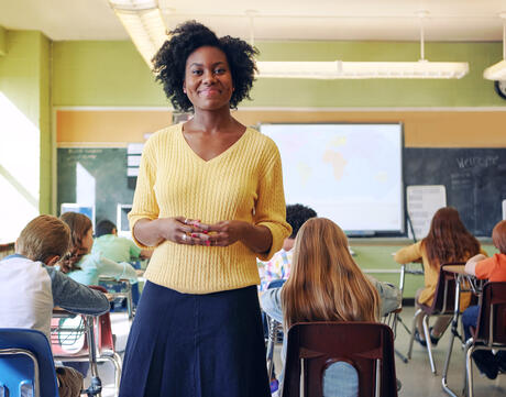 A black female educator smiles as her elementary school class writes at their desks.